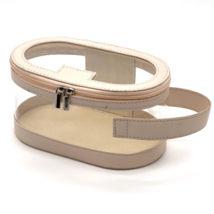 Clear oval cosmetic bag with beige faux leather trim, handle, and silver zippers