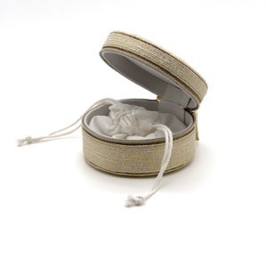 Open round jewelry box with gold fabric exterior, showing soft interior and drawstring pouch